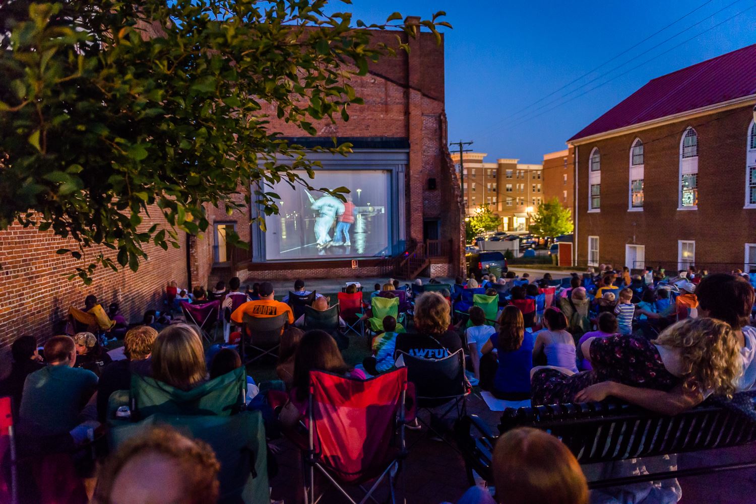 Crowd in camping chairs watching a concert on a big screen set into a stone wall